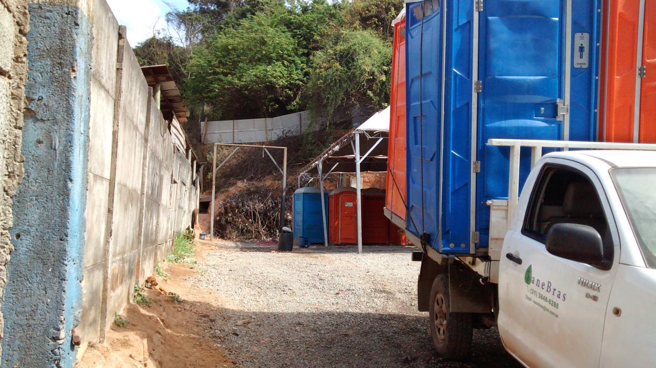 Caminhão da Sanebras carregado com banheiros químicos azuis e laranjas ao lado do pátio da empresa